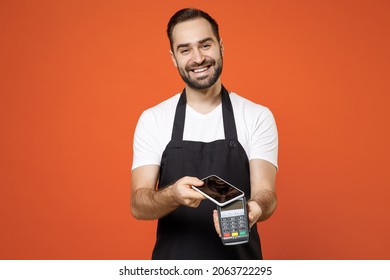 Young Man Barista Bartender Barman Employee In Apron White T-shirt Work In Coffee Shop Show Wireless Bank Payment Terminal Process Acquire Credit Mobile Phone Payment Isolated On Orange Background.