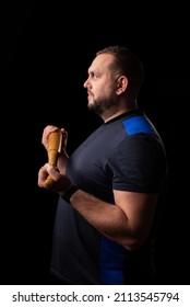 Young Man With A Baseball Bat On A Dark Background. Bouncer, Security Guard, Bodyguard Concept. Place For Text. A Large Man In A T-shirt Stands Sideways.