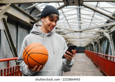 Young man basketball player with headphones holding ball using smartphone after training. Urban background. - Powered by Shutterstock