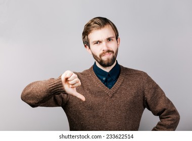 young man with a beard in brown sweater showing thumbs down sign