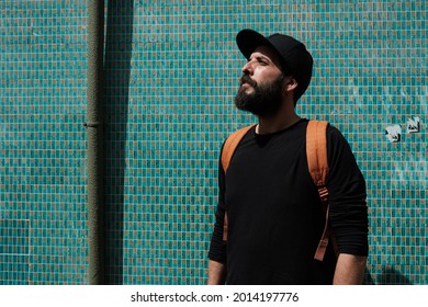 Young man with beard dressed in black with a cap discovering the city of Oporto in front of a facade covered with typical old green tiles