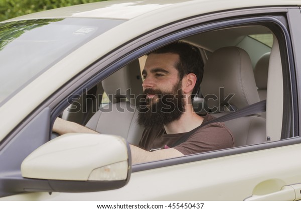 Young man with beard in the driver\'s seat of\
his car with the seat belt\
fastened.