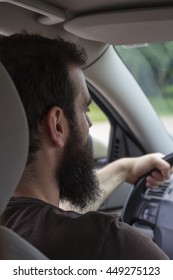 Young Man With Beard Gripping The Steering Wheel While Driving. Photo Taken Inside The Car From Behind.