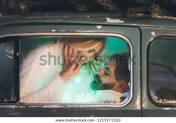 Young man with beard and his\
girlfriend in vintage car with pine tree celebrating\
Christmas