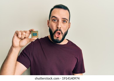 Young Man With Beard Holding Cpu Computer Processor Scared And Amazed With Open Mouth For Surprise, Disbelief Face 