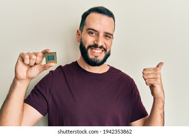 Young Man With Beard Holding Cpu Computer Processor Pointing Thumb Up To The Side Smiling Happy With Open Mouth 