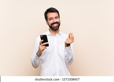 Young Man With Beard Holding A Mobile Making Money Gesture