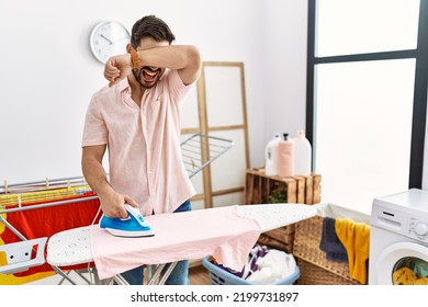 Young Man With Beard Ironing Clothes At Home Smiling Cheerful Playing Peek A Boo With Hands Showing Face. Surprised And Exited 