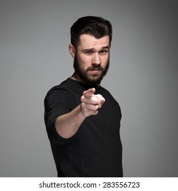 Young man with beard and mustaches, finger pointing towards the camera on a gray background