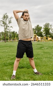 A young man with a beard performs a stretching exercise in a park, enjoying an active workout.