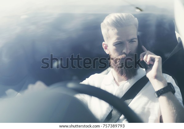 A young man with a\
beard sits at the wheel of an electric vehicle. He feels confident\
in the cabin of this car. He is wearing a seat belt. He is talking\
on the phone.