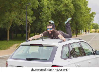 Young Man With Beard And Sunglasses Lying And Shouting On The Roof Of A Car.