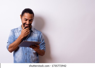 young man with beard tied hair smiles happy with hand on beard looks at his tablet and leaves the right side blank