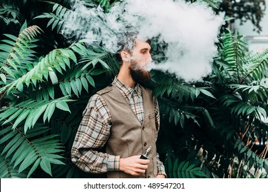 Young man with beard vaping an electronic cigarette outdoor. hipster smoke vaporizer.
