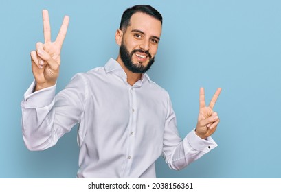 Young Man With Beard Wearing Business Shirt Smiling Looking To The Camera Showing Fingers Doing Victory Sign. Number Two. 