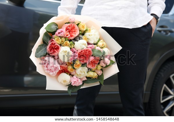 Young man with beautiful flower bouquet near car,
closeup view