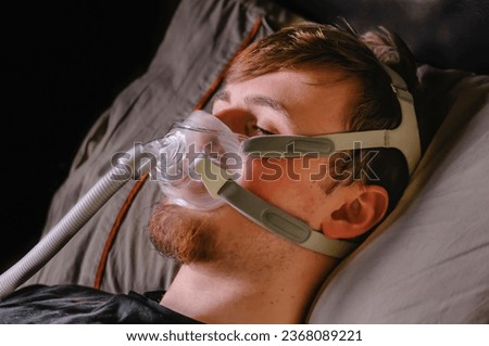 A young man in bed at night using a CPAP machine with face mask