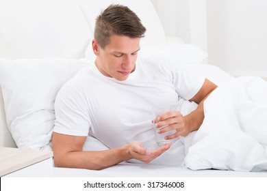 Young Man In Bed Taking Medicine With Glass Of Water