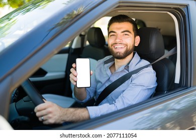 Young Man Behind The Wheel Working As A Driver On A Rideshare Mobile App And Showing His Smartphone Screen