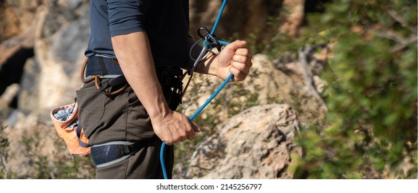 A young man belays for rock climbing in the mountains outdoors, an athlete controls on a rope during a workout, goes mountain climbing on a sunny day, close-up. - Powered by Shutterstock