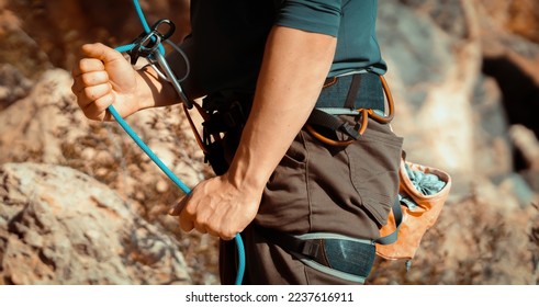 A young man belays for rock climbing in the mountains outdoors, an athlete controls on a rope during a workout, goes mountain climbing on a sunny day, close-up. - Powered by Shutterstock