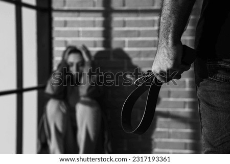 Young man with belt and his scared wife at home, closeup. Domestic violence concept