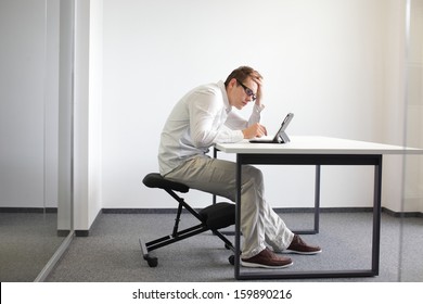Young man is bent over his tablet in his office,seating on kneeling chair  Bad sitting posture at work