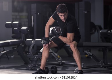 Young Man Biceps Curls Sitting. Indoors Gym Dark.