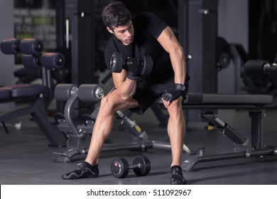 Young Man Biceps Curls Sitting. Indoors Gym Dark.