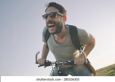 Young Man With Bicycle Having Outdoor Fun. Retro Vintage Style Image. Happy Hipster Guy Smile While Riding Bike On The Road. Cycling And Adventure Traveling Lifestyle.