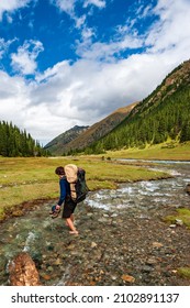 Young man with big backpack barefoot crossing river. Shoeless male backapcker in river. Karakol valley, Issyk-kul region, Ala-kul lake Terskey Alatau mountain range, Kyrgyzstan, Central Asia. - Shutterstock ID 2102891137