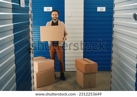Young man with big cardboard boxes into warehouse with self-storage unit