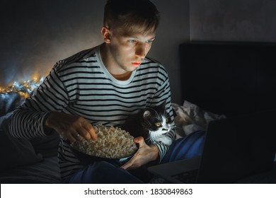 Young Man With Black Cat Watching A Movie Eating Popcorn On TV At Home. Movie Night. Relax,rest Watching A Horror Film Or Video On Screen. Background Lighting. Fun Scared Excited People On The Couch.