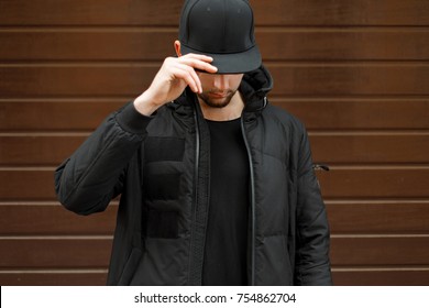 young man in a black fashionable baseball cap and a winter warm jacket posing on the street