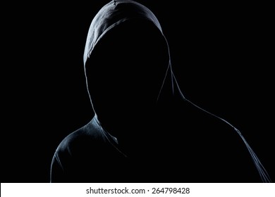 Young man in black hooded sweatshirt invisible in the night darkness, dimly lit, concepts of danger, crime, terror
