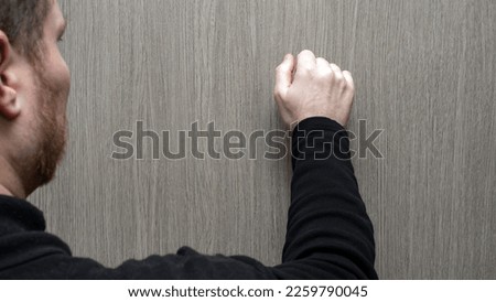 A young man in a black jacket knocks on the door. Visiting someone's home
