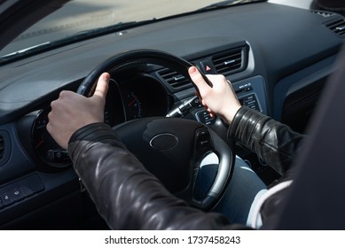 A young man in a black leather jacket sits behind the wheel of his car, on a Sunny day. Close-up of a man's hands on the steering wheel