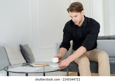 Young Man In Black Shirt Holding Cup Of Coffee While Sitting On Couch