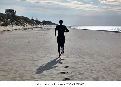 A Young Man In Black Sports Gear And Orange Sneakers Is Jogging On The Beach. Prevention Of Hypertension And Cardiovascular Disease