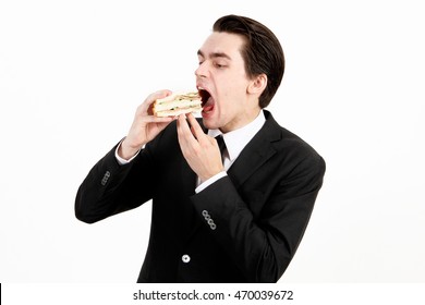 Young Man In Black Suit Eating Sandwich Against White Background