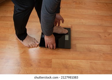 A Young Man In Black Sweatpants Weights Himself With A Scale On The Parquet.