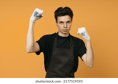 A Young Man In A Black T-shirt And Apron In Work Gloves Clenched His Hands Into Fists For A Punch