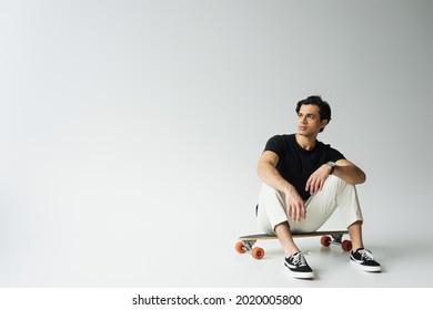 young man in black t-shirt sitting on longboard on grey