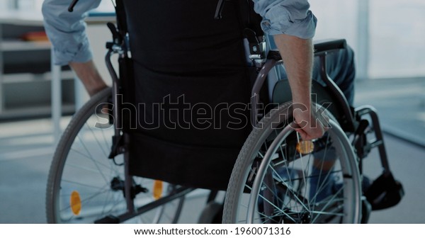 Young man in black wheelchair moving along the\
corporate office. Employee business person with disabilities\
entering office to start\
work.