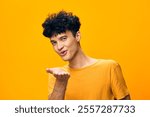 Young man blowing a kiss with an inviting smile, set against a bright yellow background that conveys warmth and positivity His casual orange shirt enhances the cheerful vibe