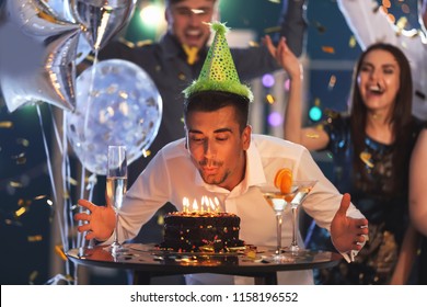 Young Man Blowing Out Candles On Birthday Cake At Party In Club