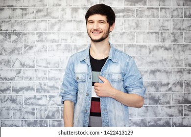 young man in blue denim jacket smiling, on the background of grey brick wall - Powered by Shutterstock