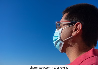 Young Man With Blue Face Mask. He Is Looking At The Sky. He Is Wearing A Salmon Colored Polo Shirt And Glasses.