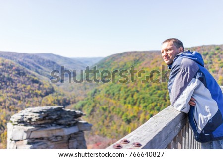 Young man in blue jacket looking at canaan valley mountains in Blackwater falls state park in West Virginia during colorful autumn fall season with yellow foliage on trees, rock cliff at Lindy Point