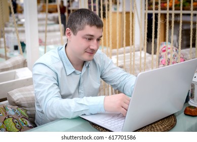 Young man in blue shirt looking at laptop sitting at a table in a cafe
